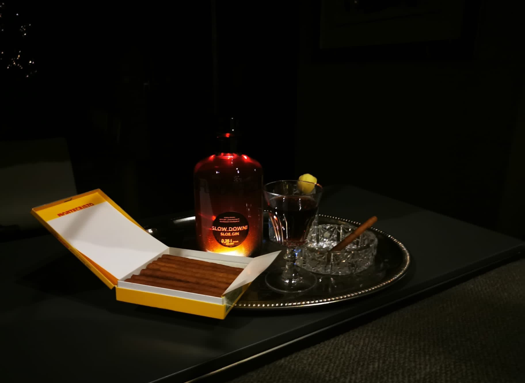 Auf einem Silbertablett stehen eine bunte Flasche, ein Aschenbecher und eine Schachtel mit Zigarillos