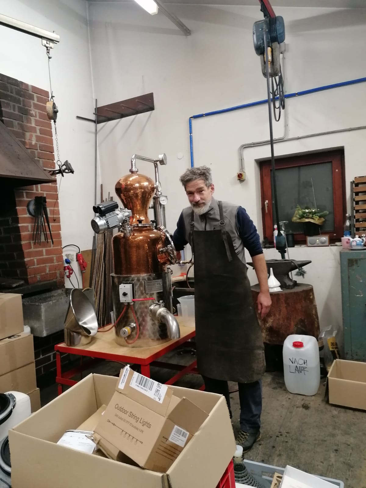 Ein Mann steht in einer Werkstatt vor einer Destillationsanlage