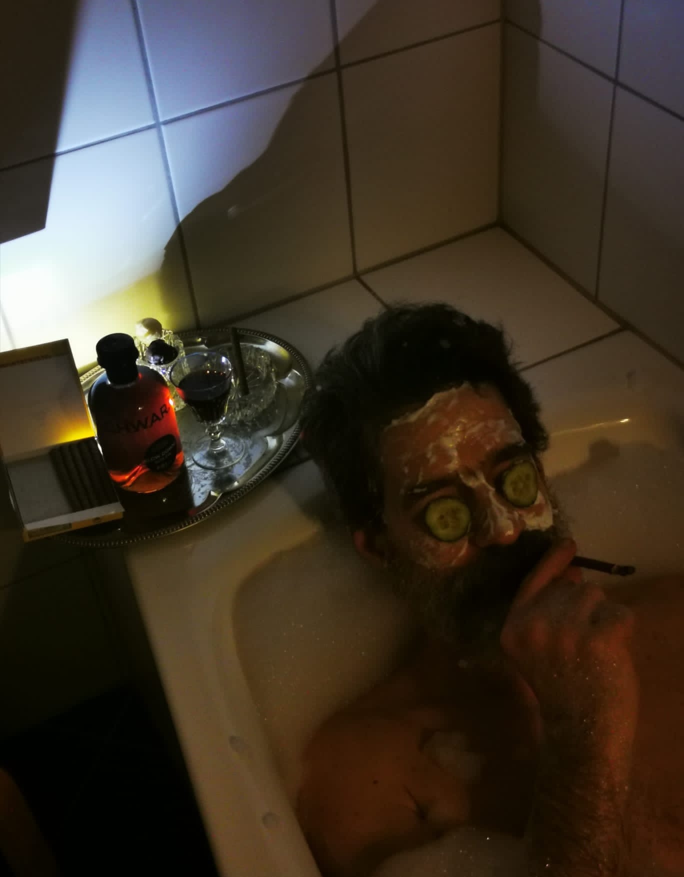 Ludwig Schwarz Mann liegt in einer Badewanne. Er raucht einen Zigarillo und hat Gurkenscheiben auf den Augen