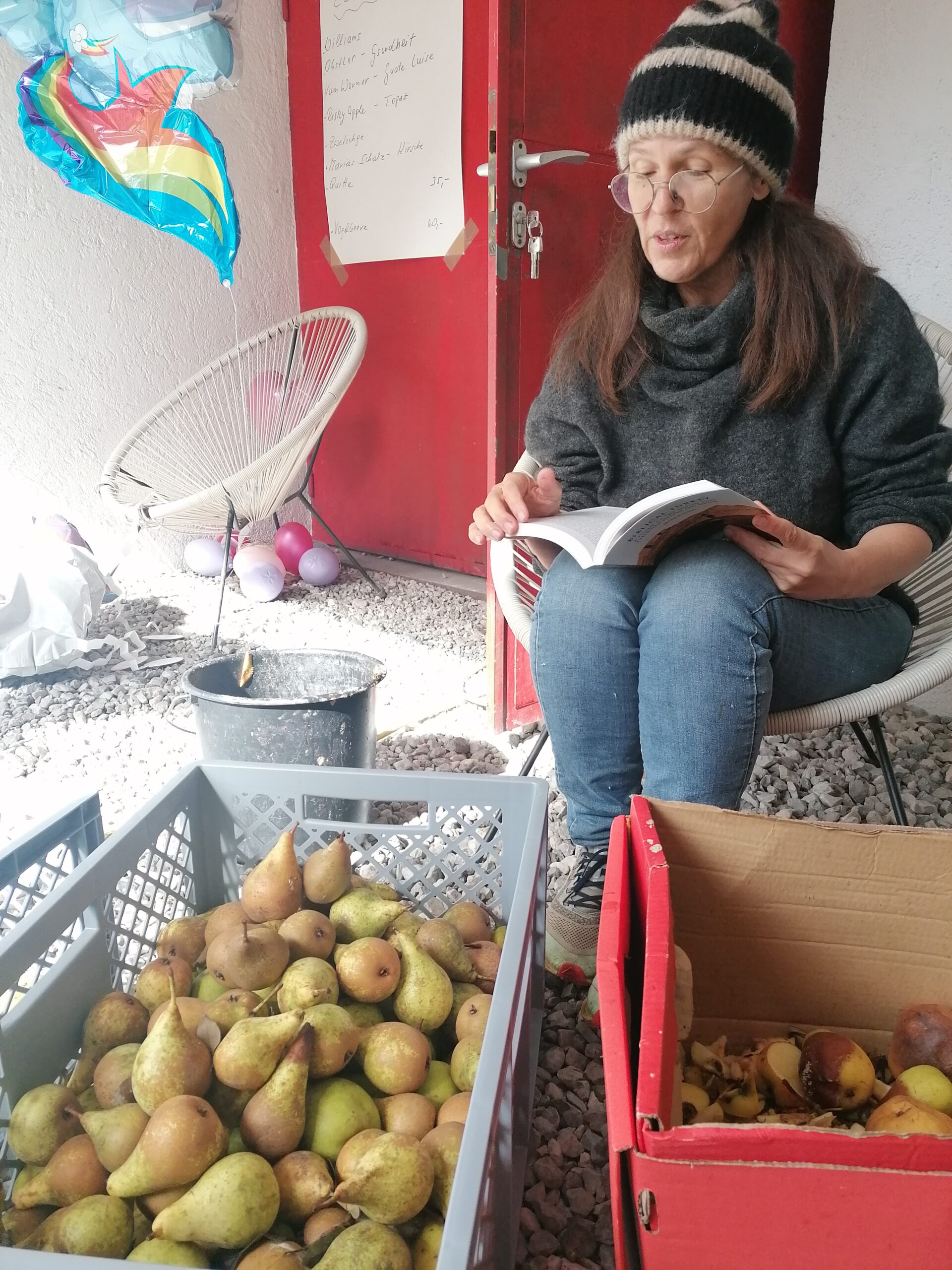 Sonja Schwarz-Dum Frau sitz mit einem Buch in der Hand vor einer Kiste voller Birnen